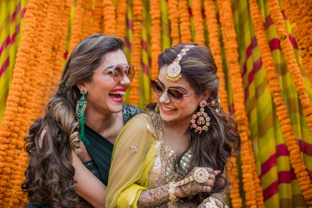 A bride wearing pretty gota jewellery with her sister on her mehndi ceremony 