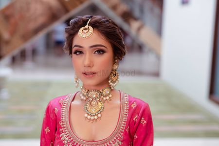 Photo of A bride in hot pink lehenga with a gold choker on her mehendi day
