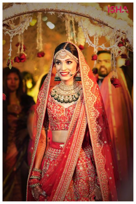 bride entering in a red lehenga with green jewellery