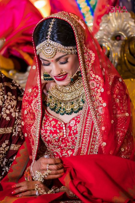 Photo of bride in red and gold lehenga with contrasting green jewellery