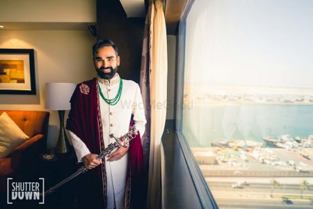Photo of groom in white sherwani with stole and sword
