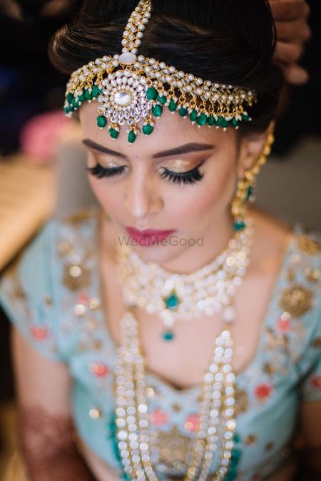Photo of bride with gold eye makeup and green kundan mathapatti