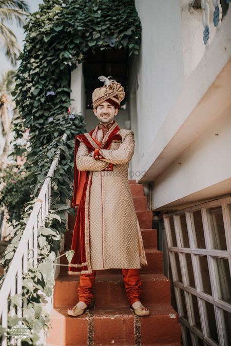 A groom in a gold sherwani with a maroon velvet stole. 