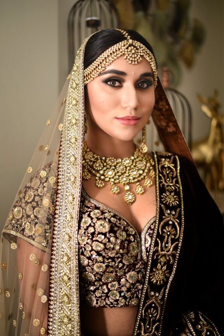 A bride in maroon and gold velvet lehenga