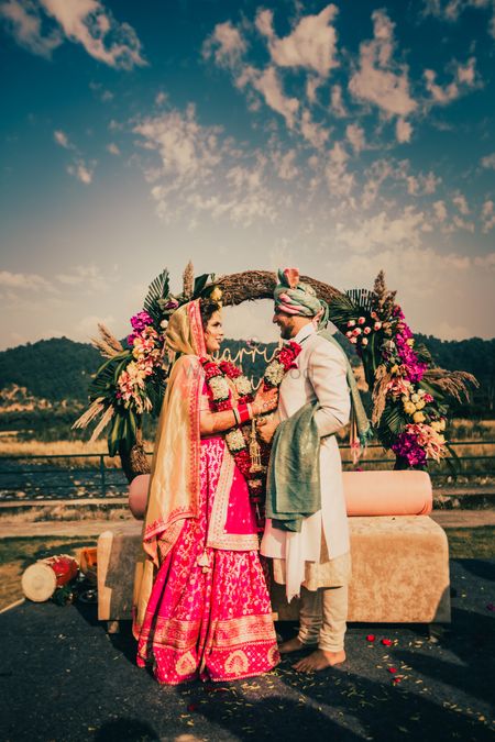 Photo of pretty couple jaimala shot with the backdrop of the hills