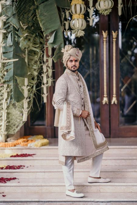 A groom dressed in white and gold sherwani on his wedding day