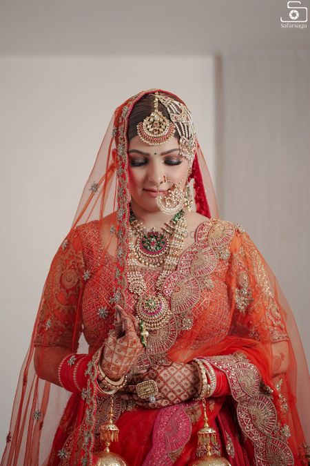 Photo of a bride wearing red lehenga and oversized jewellery.