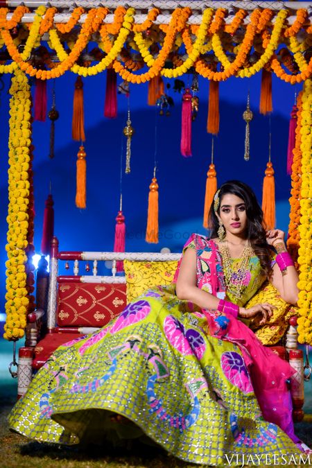 South Indian bride in a multi-colored lehenga posing on a jhoola.