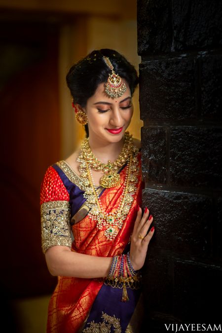A coy South Indian bride wearing a red and blue saree with temple jewellery