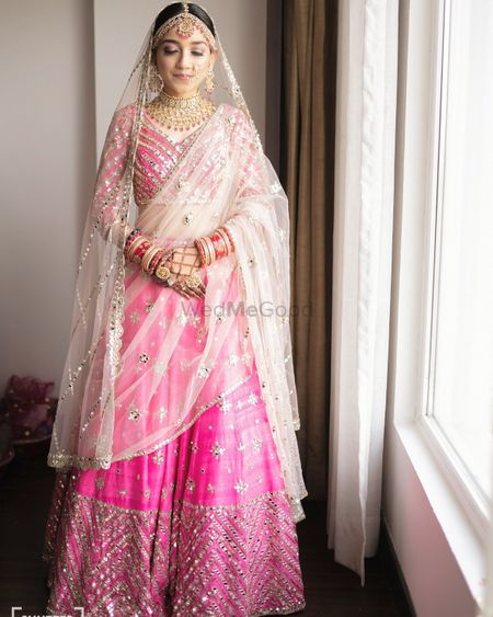 Bride wearing a bright pink lehenga with a white dupatta.