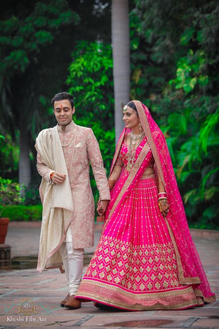 A candid shot of a bride and a groom dressed in different shades of pink.