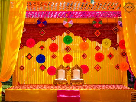 Mehndi decor with yellow backdrop decorated with paper flowers and kites.