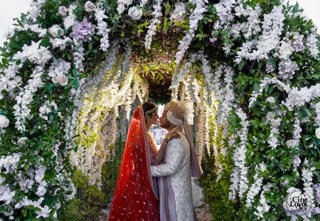 Photo of couple kissing against heavy floral mandap decor