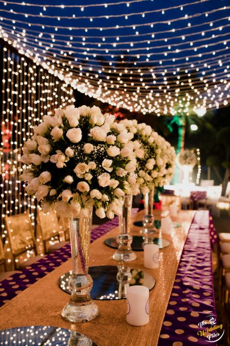 Tall floral vases used as table centrepieces with fairy light in the backdrop.