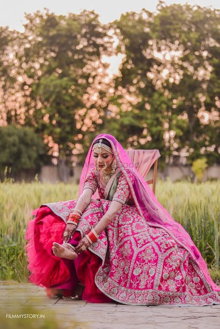 Photo of bride adjusting her bright pink can can lehenga