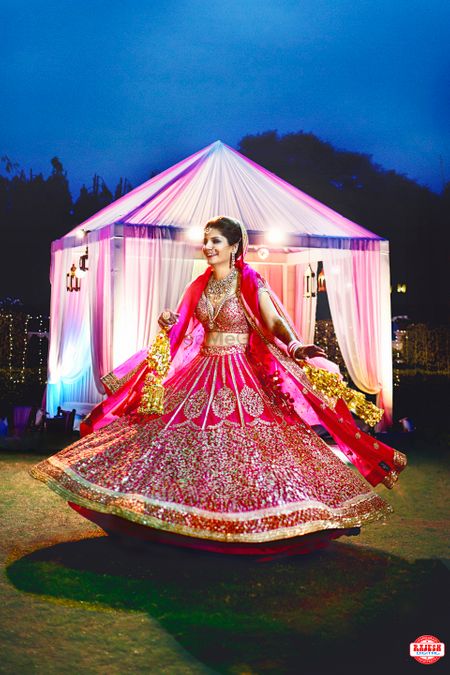Photo of Bride Twirling in Deep Pink and Gold Wedding Lehenga