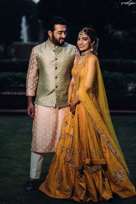 Photo of Candid shot of bride and groom dressed in yellow and pastel hues respectively.