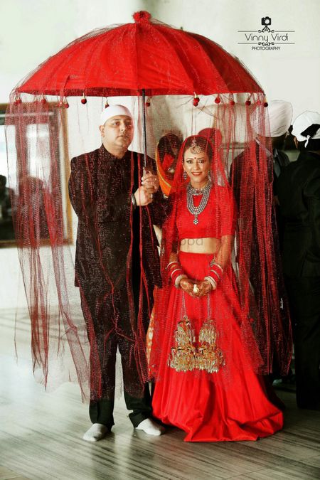 Bride in Monotone Red Lehenga Entering under Umbrella