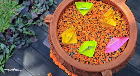 Earthen pot with floating petals and paper boats