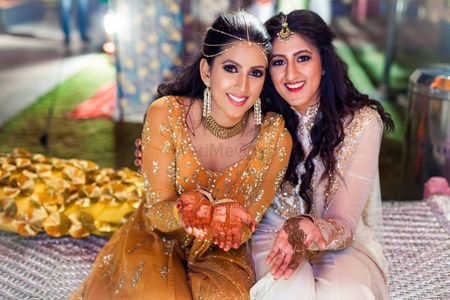 Photo of Bride in marigold anarkali with sister on mehendi