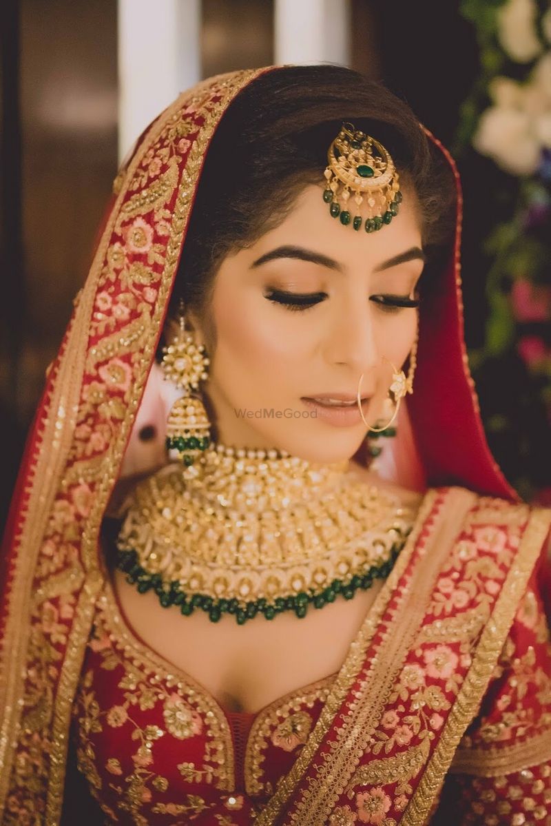 Photo of Bride in red and gold cold shoulder lehenga with green jewellery