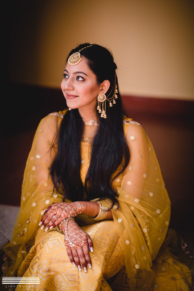 Photo of A bride in a gold mehendi outfit with waterfall earrings